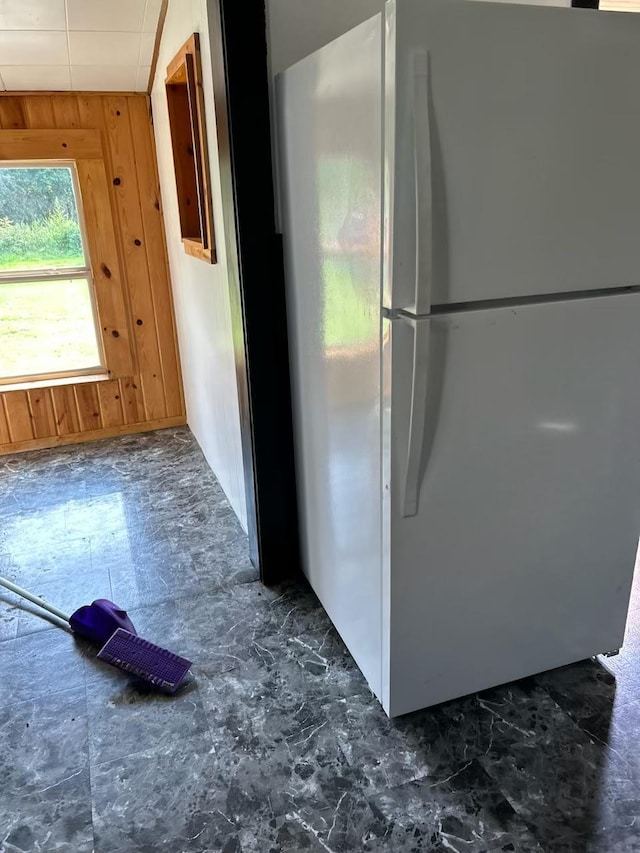 kitchen featuring dark tile patterned flooring, wooden walls, and white refrigerator