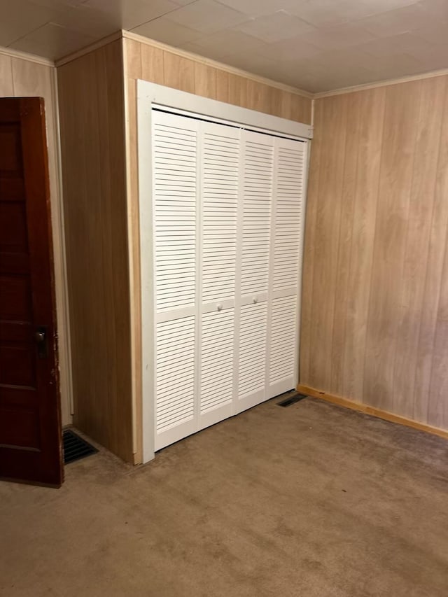 unfurnished bedroom with carpet, wooden walls, and a closet