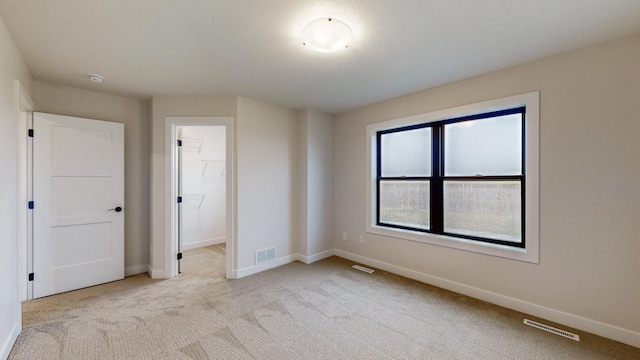 unfurnished bedroom with light colored carpet, a closet, and a spacious closet