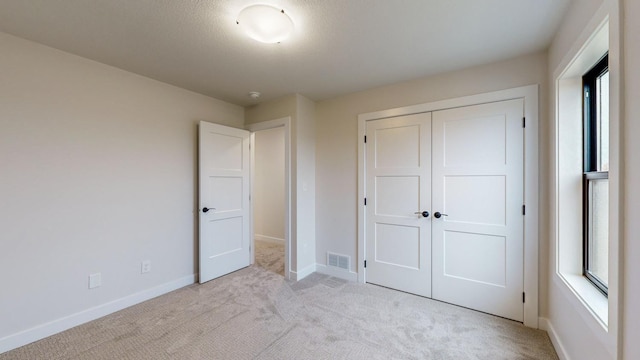 unfurnished bedroom with light carpet, a closet, and a textured ceiling