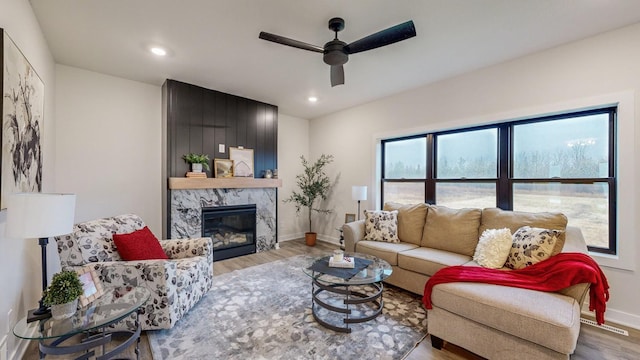 living room with a premium fireplace, ceiling fan, wood-type flooring, and a healthy amount of sunlight