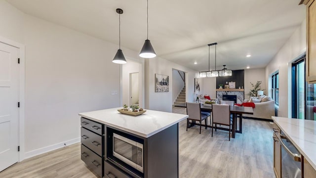 kitchen featuring a center island, stainless steel microwave, pendant lighting, a fireplace, and light wood-type flooring