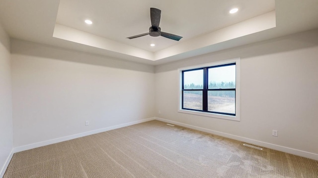 carpeted empty room featuring ceiling fan and a raised ceiling