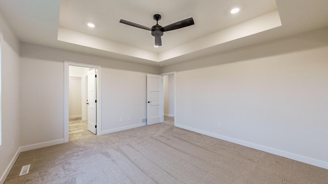 unfurnished bedroom featuring light carpet, ceiling fan, and a raised ceiling