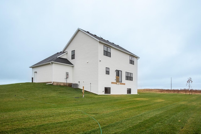 rear view of house with central AC unit and a yard