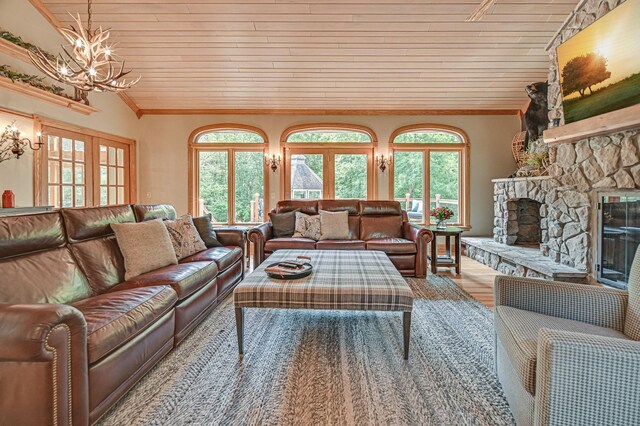 living room featuring an inviting chandelier, a stone fireplace, wood-type flooring, ornamental molding, and lofted ceiling