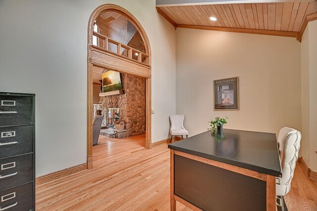 office space with vaulted ceiling, wooden ceiling, a stone fireplace, light hardwood / wood-style floors, and ornamental molding