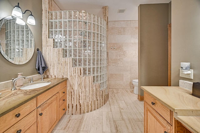 bathroom featuring a shower, tile walls, toilet, and vanity