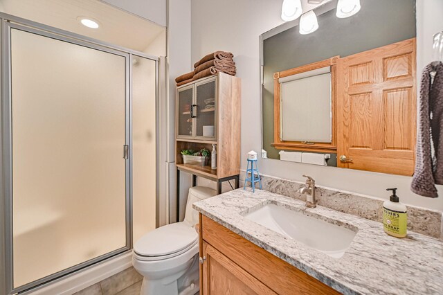 bathroom with a shower with shower door, toilet, vanity, and tile patterned floors