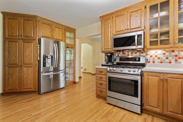 kitchen with appliances with stainless steel finishes, backsplash, and light hardwood / wood-style flooring