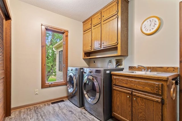 laundry room featuring sink, cabinets, a textured ceiling, washer and clothes dryer, and light hardwood / wood-style floors