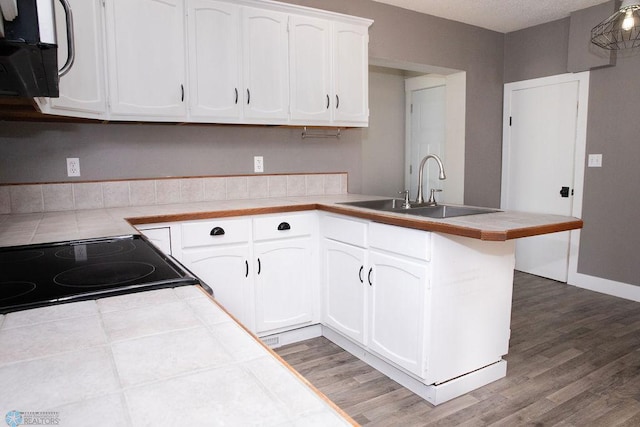 kitchen featuring a peninsula, tile counters, white cabinetry, and a sink