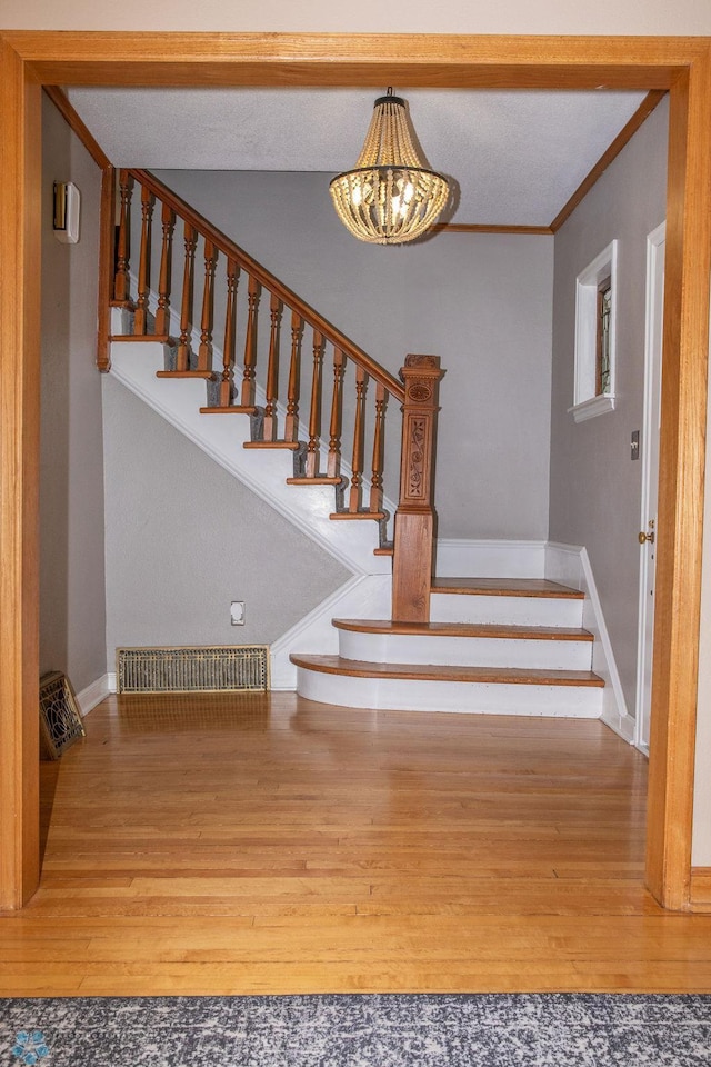 stairway with crown molding, visible vents, an inviting chandelier, wood finished floors, and baseboards