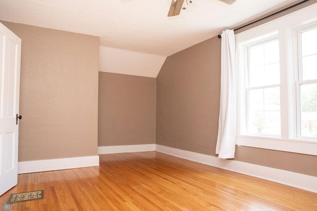 bonus room with lofted ceiling, visible vents, light wood-style floors, a ceiling fan, and baseboards