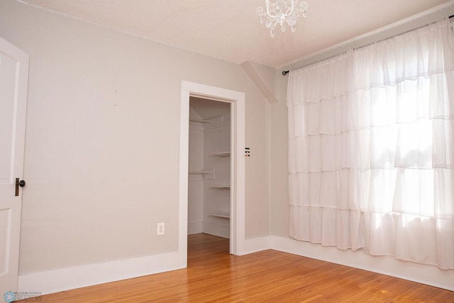 spare room featuring an inviting chandelier, baseboards, and wood finished floors