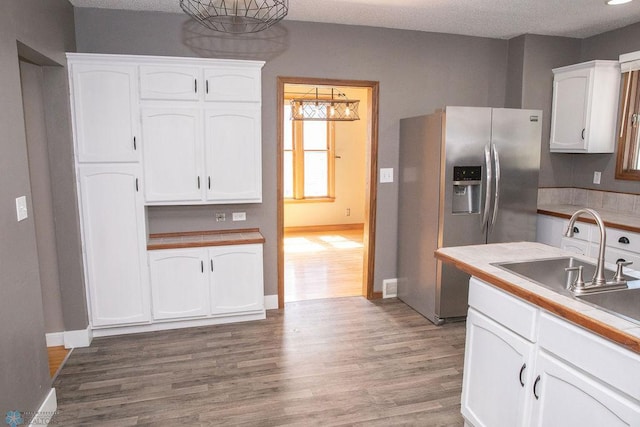 kitchen with stainless steel fridge, baseboards, white cabinets, wood finished floors, and a sink