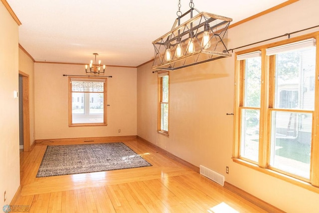 unfurnished dining area featuring visible vents, baseboards, wood finished floors, crown molding, and a notable chandelier