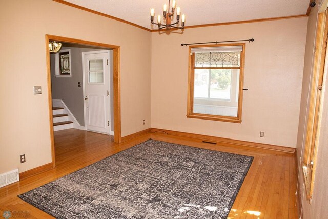 spare room with ornamental molding, a chandelier, visible vents, and wood finished floors