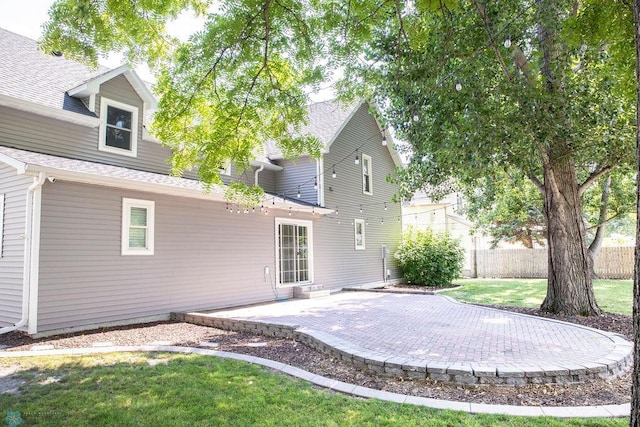 rear view of property with a yard, roof with shingles, a patio area, and fence