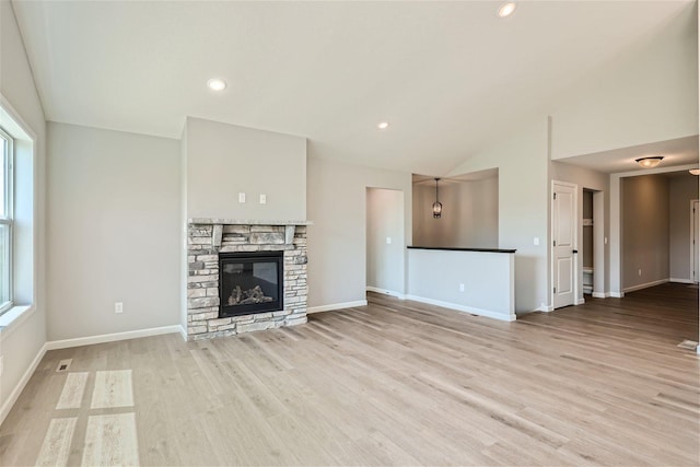 unfurnished living room with a stone fireplace, vaulted ceiling, and light hardwood / wood-style floors