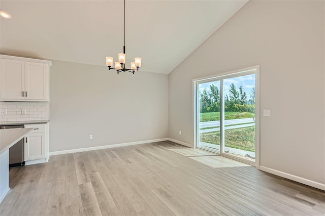 unfurnished dining area featuring an inviting chandelier, light wood-type flooring, and high vaulted ceiling