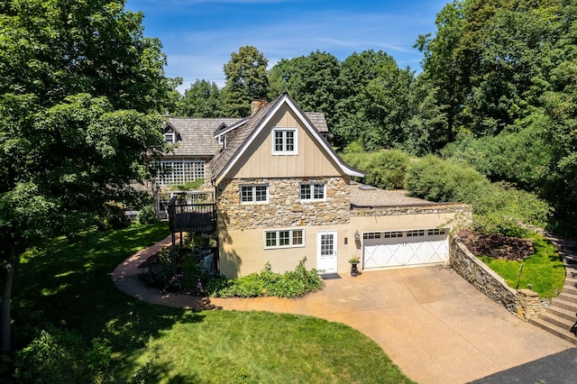 view of side of property featuring driveway, a chimney, a garage, stone siding, and board and batten siding