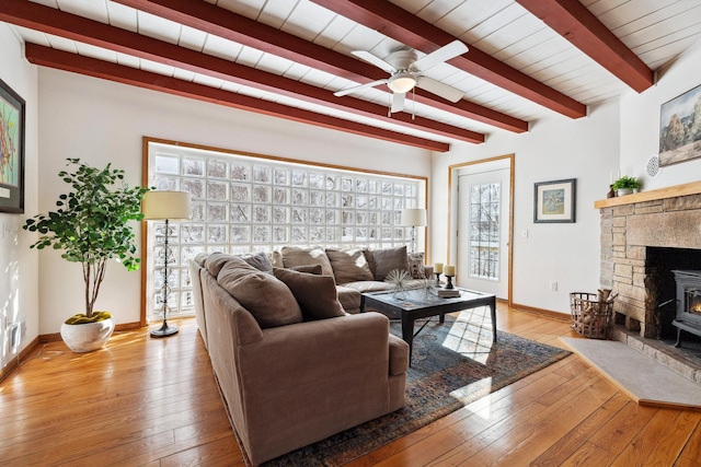 living area with beam ceiling, hardwood / wood-style flooring, baseboards, ceiling fan, and a wood stove