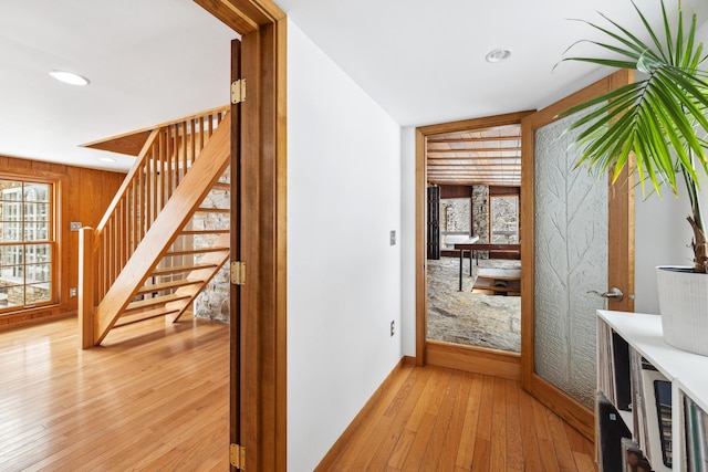 corridor featuring light wood finished floors, recessed lighting, wood walls, and stairs