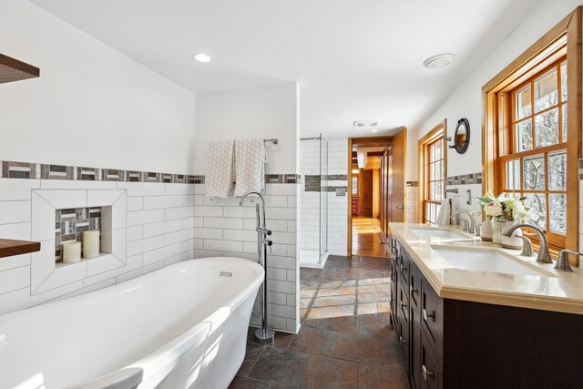 bathroom featuring a sink, a freestanding bath, stone tile flooring, and double vanity