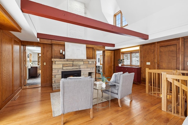 living area featuring beamed ceiling, a stone fireplace, wood walls, and light wood finished floors