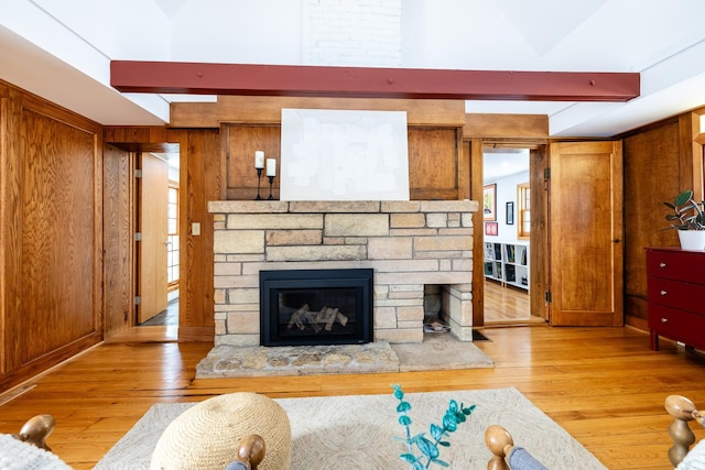 living area with wooden walls, light wood-style flooring, a stone fireplace, and beamed ceiling