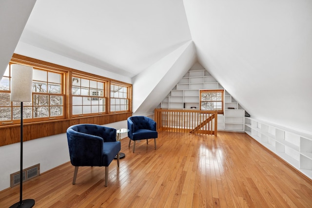 sitting room with built in features, visible vents, wood-type flooring, and vaulted ceiling