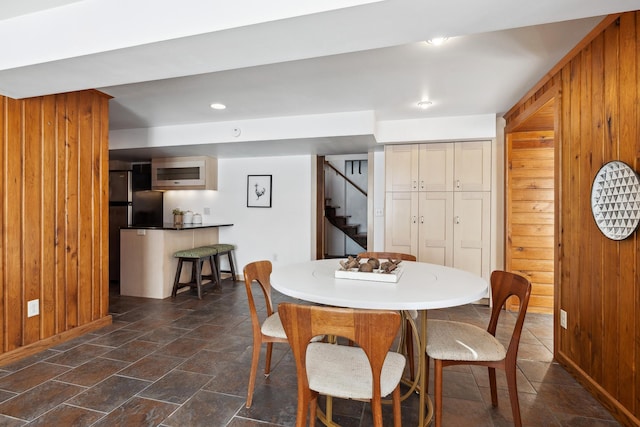 dining area featuring baseboards, recessed lighting, stairs, wood walls, and stone finish flooring