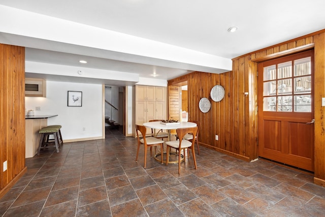 dining area with wood walls, stone finish flooring, stairs, and baseboards