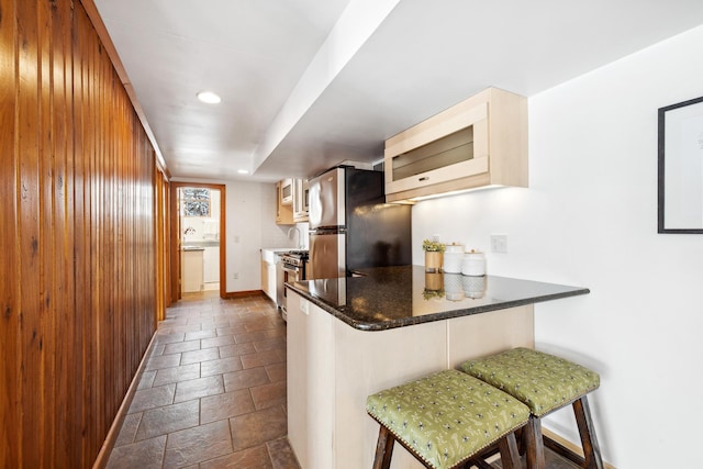 kitchen with a kitchen bar, stone tile floors, stainless steel appliances, a peninsula, and baseboards