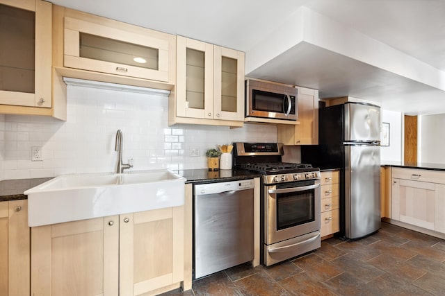 kitchen featuring a sink, stainless steel appliances, stone finish floor, dark countertops, and backsplash