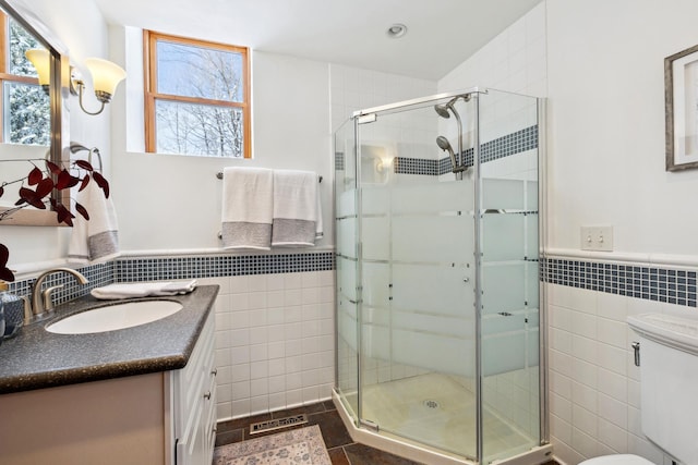 bathroom with visible vents, a shower stall, toilet, vanity, and tile walls