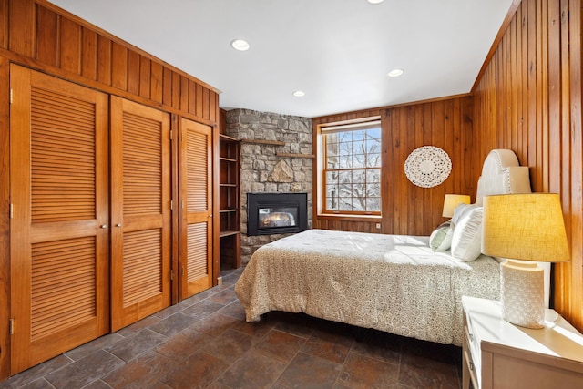 bedroom with wooden walls, recessed lighting, stone tile flooring, a stone fireplace, and a closet