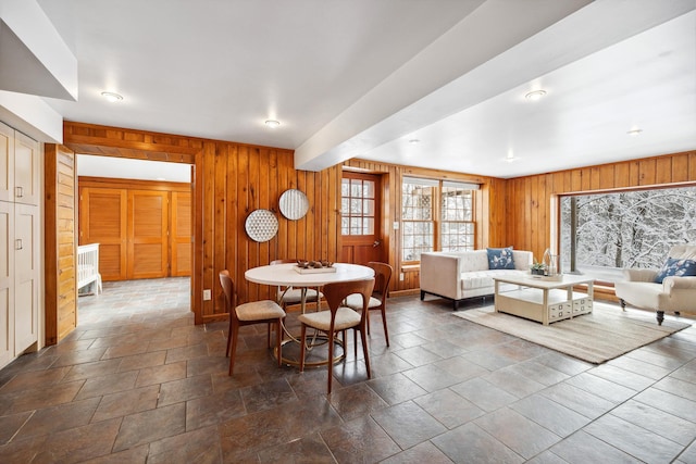 dining room featuring beam ceiling, wood walls, and stone finish flooring