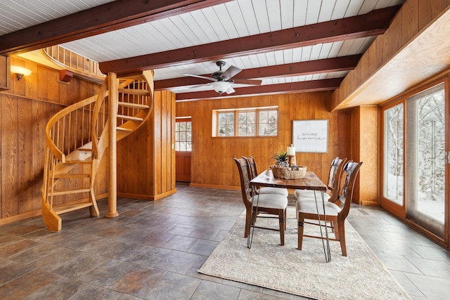 dining space featuring stairs, beam ceiling, baseboards, and wood walls