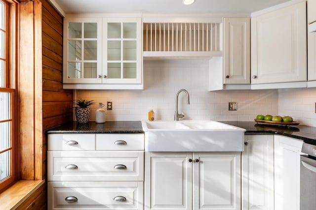 kitchen featuring backsplash, glass insert cabinets, dark stone counters, white cabinets, and a sink