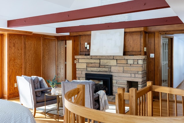 living room with beam ceiling, wooden walls, a fireplace, and light wood finished floors