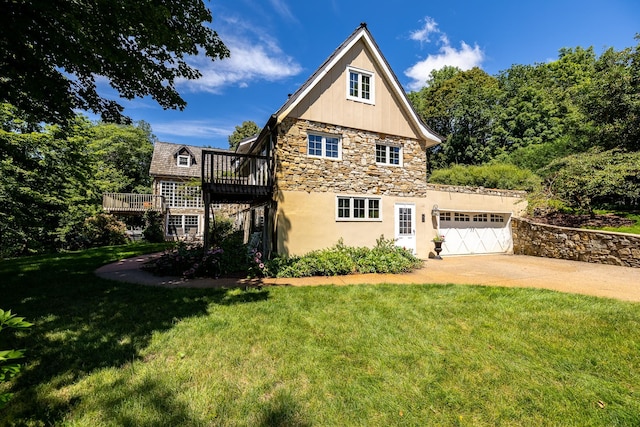 view of side of property featuring a lawn, a deck, driveway, stone siding, and an attached garage