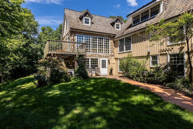 rear view of property with stone siding, board and batten siding, a yard, and a deck