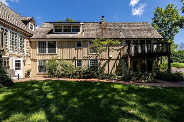 rear view of house featuring a lawn, a deck, stone siding, board and batten siding, and a chimney