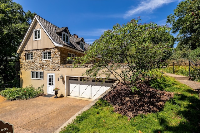 view of front of property featuring fence, driveway, a garage, stone siding, and board and batten siding