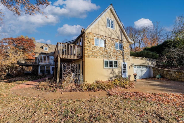 view of property exterior featuring board and batten siding, driveway, a deck, stone siding, and an attached garage