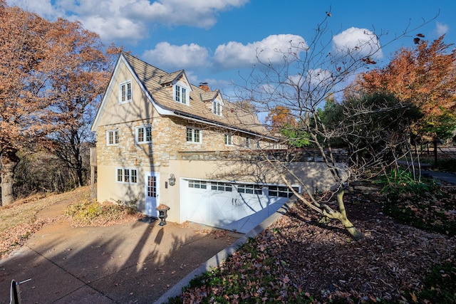 view of home's exterior with an attached garage, stucco siding, a chimney, concrete driveway, and stone siding