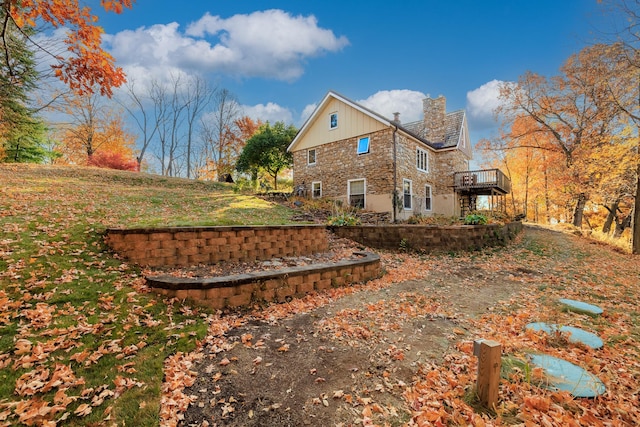 rear view of property with stone siding, a deck, and a chimney