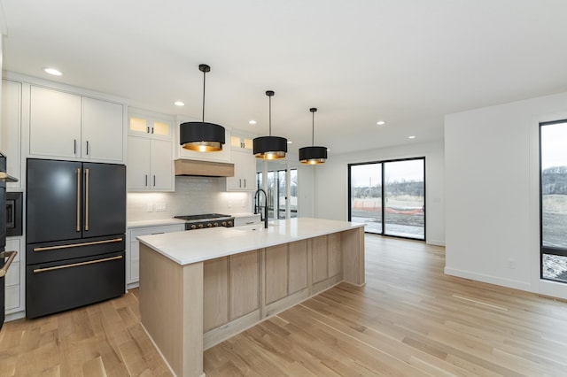 kitchen with sink, paneled built in refrigerator, a kitchen island with sink, white cabinetry, and decorative light fixtures